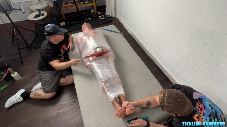 Man Wrapped in Cellophane Endures Tickling from 2 Men